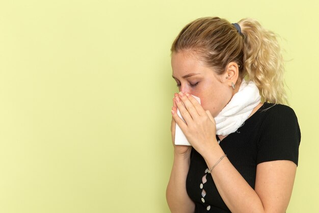 Vue de face jeune femme avec une serviette blanche autour de sa gorge se sentir très malade et mal nettoyer son nez sur le mur vert maladie maladie femelle couleur santé