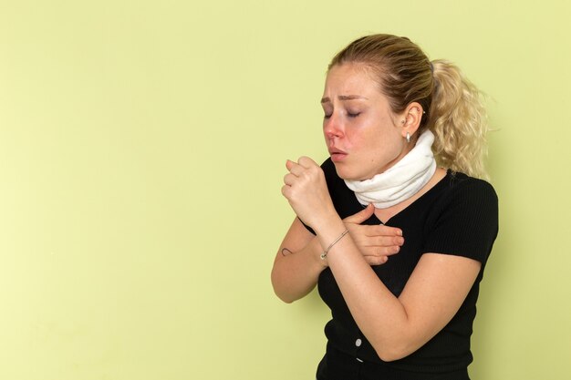 Vue de face jeune femme avec une serviette blanche autour de sa gorge se sentir très malade et mal toux sur le mur vert maladie maladie couleur femme