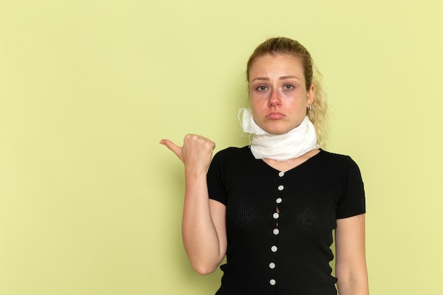 Vue de face jeune femme avec une serviette blanche autour de sa gorge se sentir très malade et malade posant sur le bureau vert clair maladie de la santé féminine