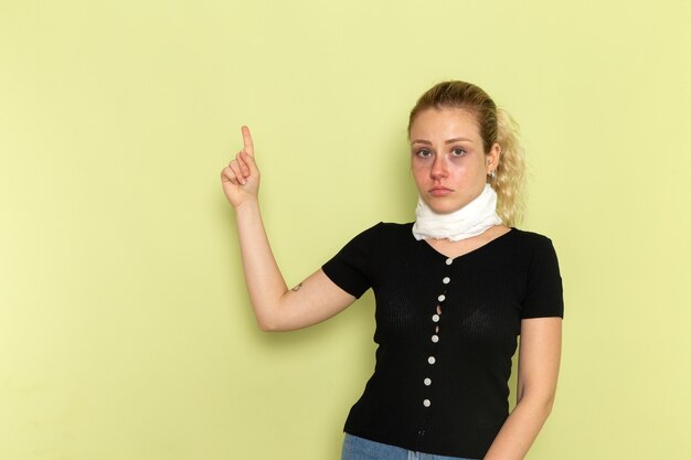 Vue de face jeune femme avec une serviette blanche autour de sa gorge se sentir très malade et malade posant sur le modèle de maladie de bureau vert clair maladie médecine santé