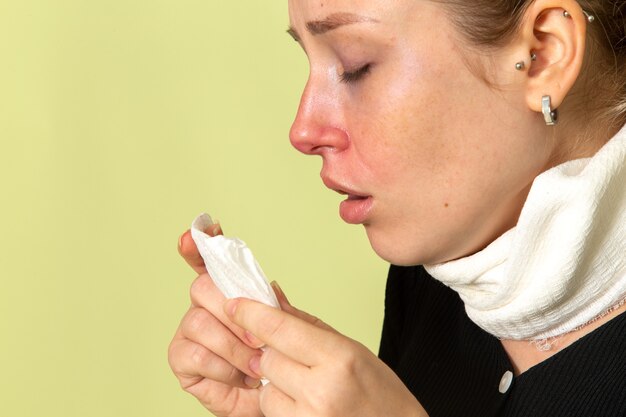 Vue de face jeune femme avec une serviette blanche autour de sa gorge se sentir très malade et malade snezzing sur mur vert maladie maladie femme santé fille