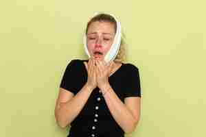 Photo gratuite vue de face jeune femme avec une serviette blanche autour de sa tête se sentir très malade et malade de mal de dents éternuer sur mur vert maladie maladie femme santé fille