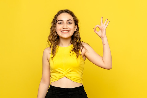 Vue de face de la jeune femme souriant joyeusement sur le mur jaune