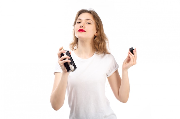 Une vue de face jeune femme en t-shirt blanc à l'aide d'un tube de parfum noir sur le blanc