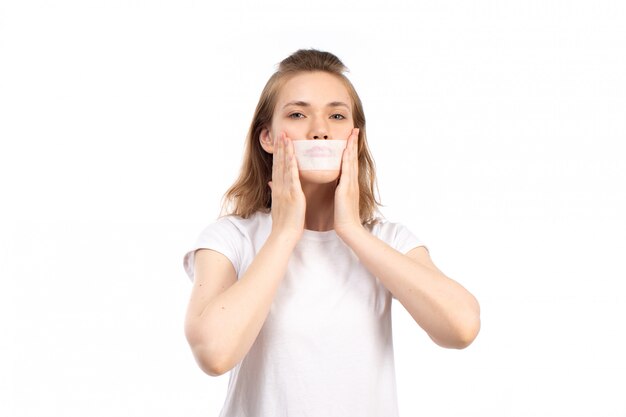 Une vue de face jeune femme en t-shirt blanc avec un bandage blanc autour de sa bouche sur le blanc