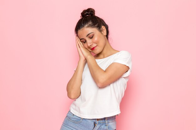 Une vue de face jeune femme en t-shirt blanc et blue-jeans essayant de faire semblant de dormir avec sourire