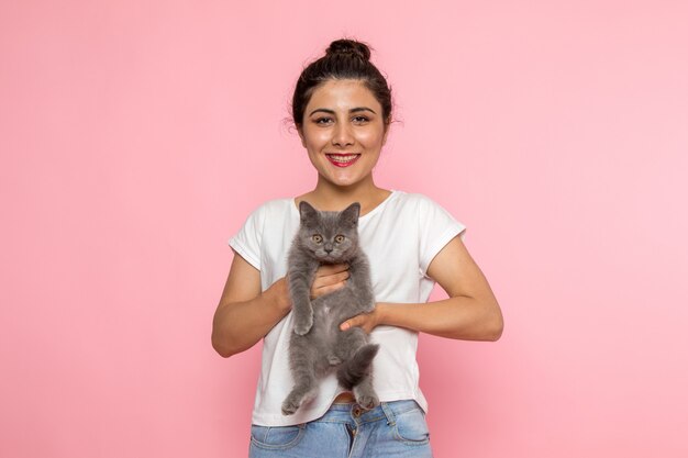 Une vue de face jeune femme en t-shirt blanc et blue-jeans tenant chaton gris