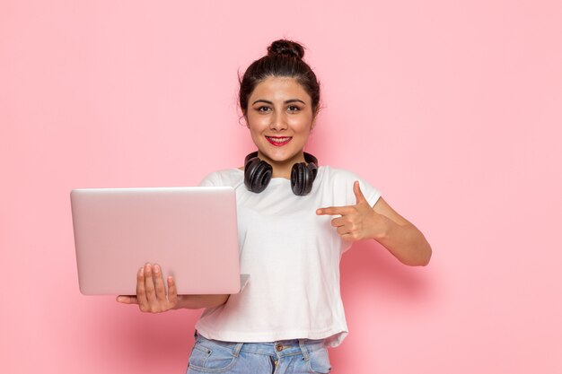 Une vue de face jeune femme en t-shirt blanc et blue-jeans tenant un ordinateur portable avec sourire