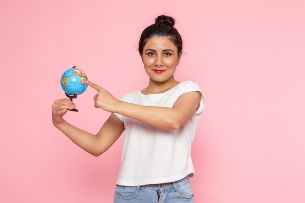 Une vue de face jeune femme en t-shirt blanc et blue-jeans tenant petit globe