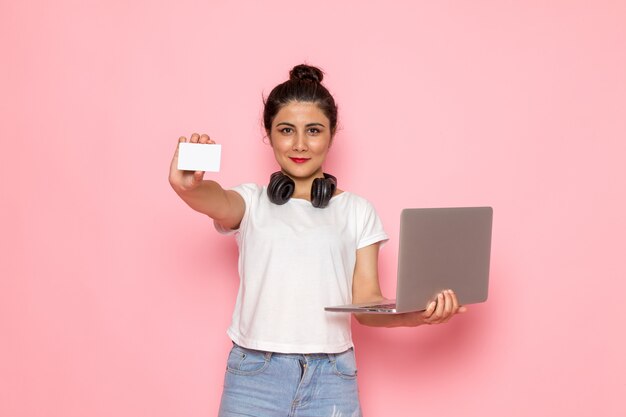 Une vue de face jeune femme en t-shirt blanc et jean bleu à l'aide d'un ordinateur portable avec sourire