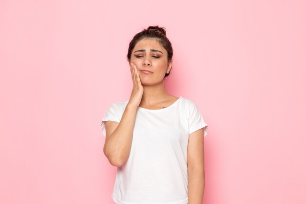 Une vue de face jeune femme en t-shirt blanc et jean bleu ayant mal aux dents