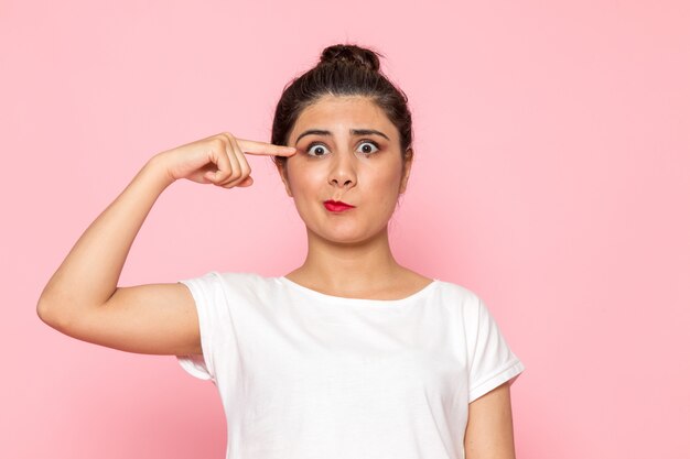 Une vue de face jeune femme en t-shirt blanc et jean bleu posant avec drôle d'expression