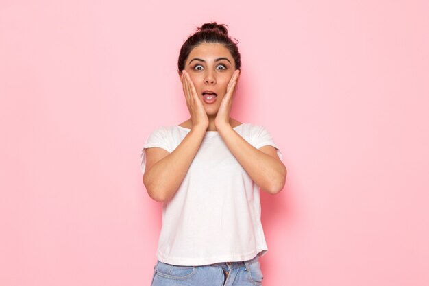 Une vue de face jeune femme en t-shirt blanc et jean bleu posant avec une expression surprise