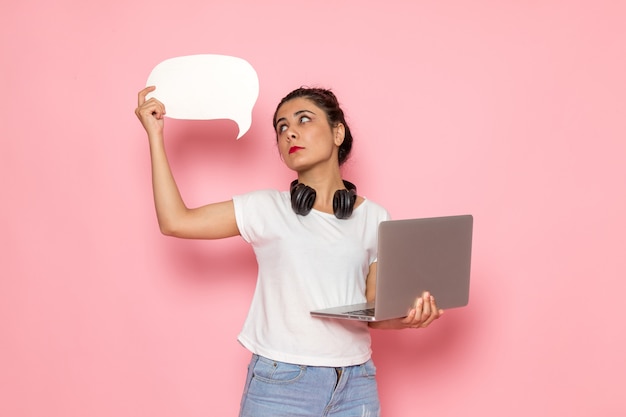 Une vue de face jeune femme en t-shirt blanc et jean bleu tenant un ordinateur portable et panneau blanc