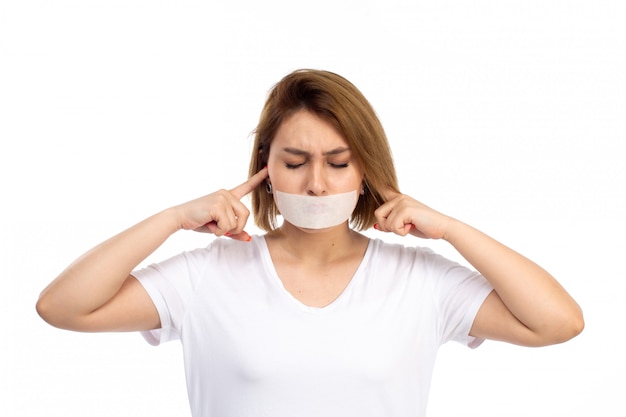 Une Vue De Face Jeune Femme En T-shirt Blanc Et Jean Noir Portant Un Bandage Blanc Autour De Sa Bouche Fermant Ses Oreilles Sur Le Blanc