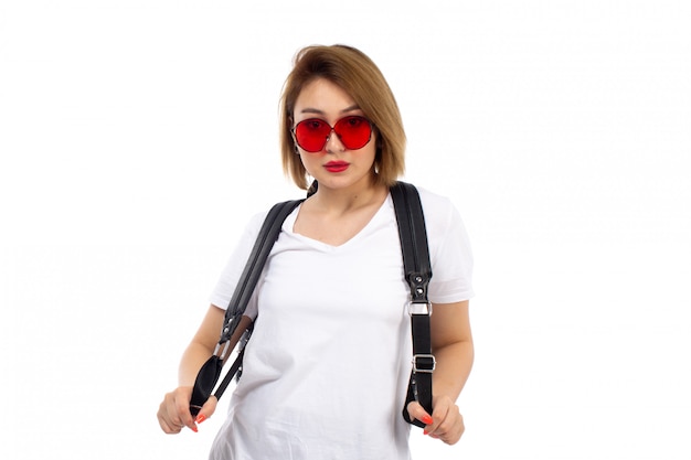 Une vue de face jeune femme en t-shirt blanc lunettes de soleil rouges sac noir sur le blanc