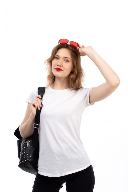 Une vue de face jeune femme en t-shirt blanc lunettes de soleil rouges sac noir souriant sur le blanc