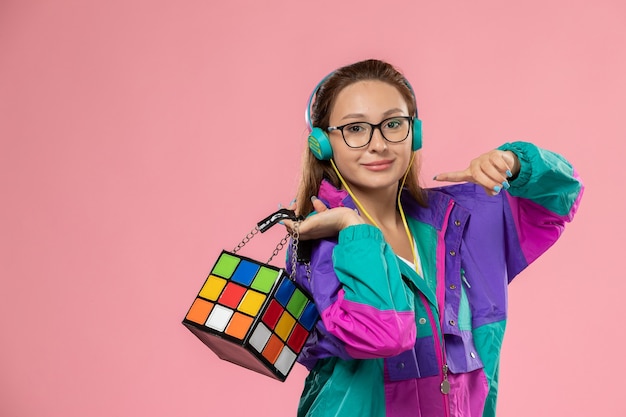 Vue de face jeune femme en t-shirt blanc manteau de couleur à écouter de la musique via des écouteurs avec le sourire sur le fond clair