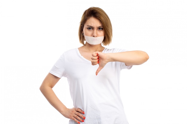 Une vue de face jeune femme en t-shirt blanc portant un bandage blanc autour de sa bouche mécontent sur le blanc