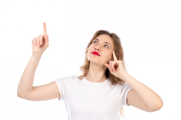 Une vue de face jeune femme en t-shirt blanc posant à la recherche dans le ciel en pensant sur le blanc