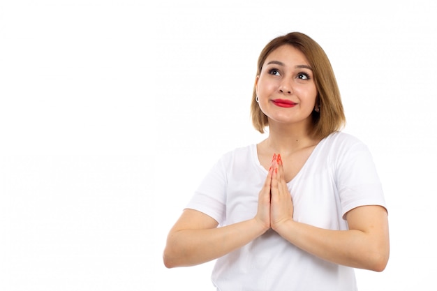 Une vue de face jeune femme en t-shirt blanc posant souriant priant sur le blanc