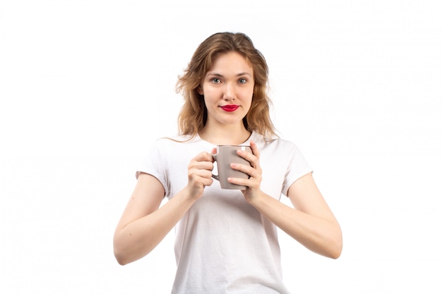 Une vue de face jeune femme en t-shirt blanc souriant tenant une tasse sur le blanc