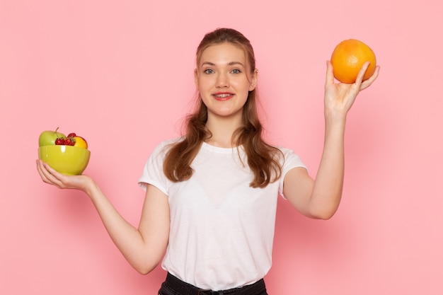 Vue de face de la jeune femme en t-shirt blanc tenant la plaque avec des fruits frais souriant