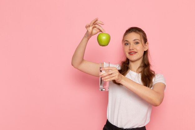 Vue de face de la jeune femme en t-shirt blanc tenant une pomme verte fraîche et un verre d'eau
