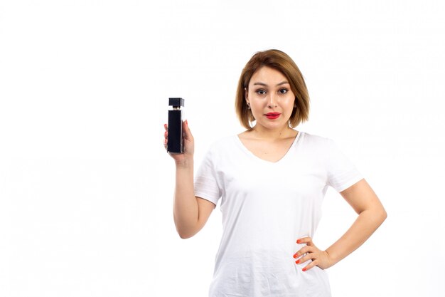 Une vue de face jeune femme en t-shirt blanc tenant un tube de parfum noir sur le blanc