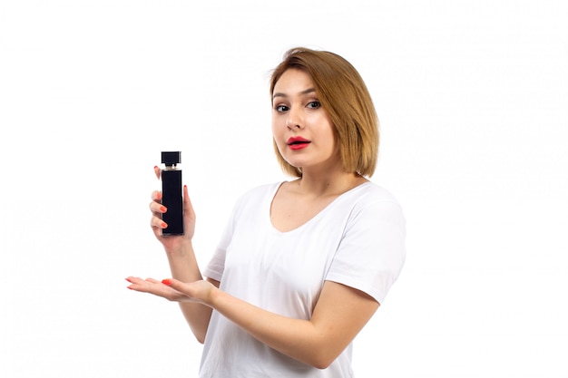 Une vue de face jeune femme en t-shirt blanc tenant un tube de parfum noir sur le blanc