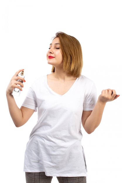Une vue de face jeune femme en t-shirt blanc tenant un tube de parfum noir en utilisant sur le blanc