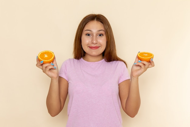 Vue de face jeune femme en t-shirt rose et blue-jeans tenant orange avec sourire
