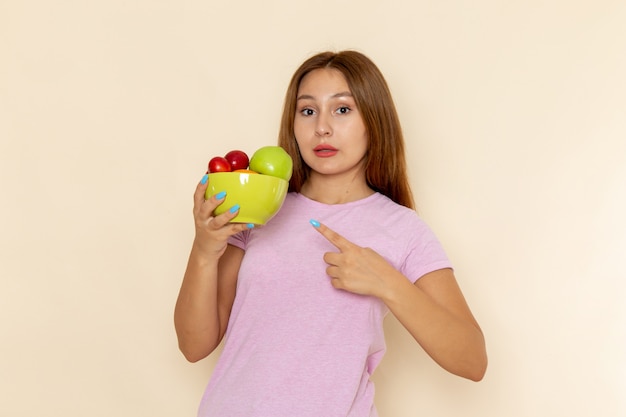 Vue de face jeune femme en t-shirt rose et blue-jeans tenant la plaque avec des fruits