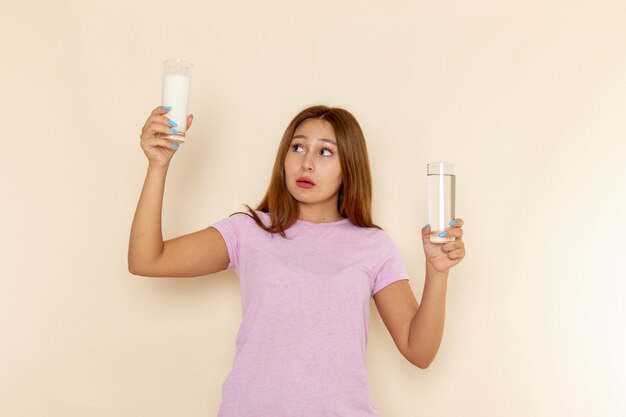 Vue de face jeune femme en t-shirt rose et jean bleu tenant de l'eau et du lait sur fond gris