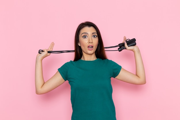 Vue de face jeune femme en t-shirt vert tenant la corde à sauter sur le mur rose taille sport exercices d'entraînement beauté athlète mince