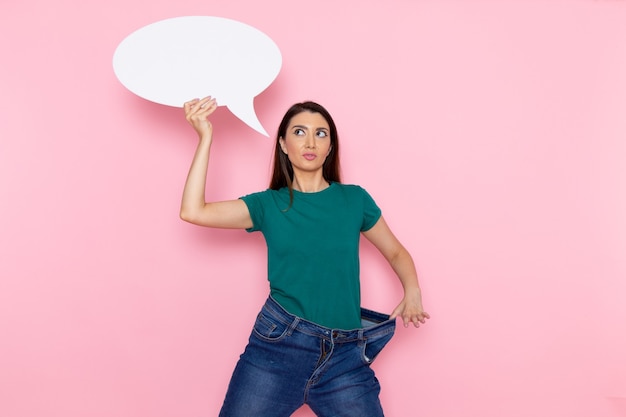 Photo gratuite vue de face jeune femme en t-shirt vert tenant une pancarte blanche sur le mur rose taille sport exercice d'entraînement beauté athlète mince