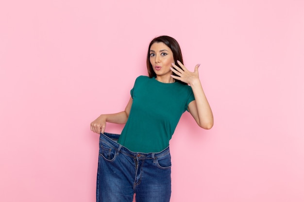 Vue de face jeune femme en t-shirt vert vérifiant sa taille sur le mur rose taille sport exercices d'entraînement beauté femme mince