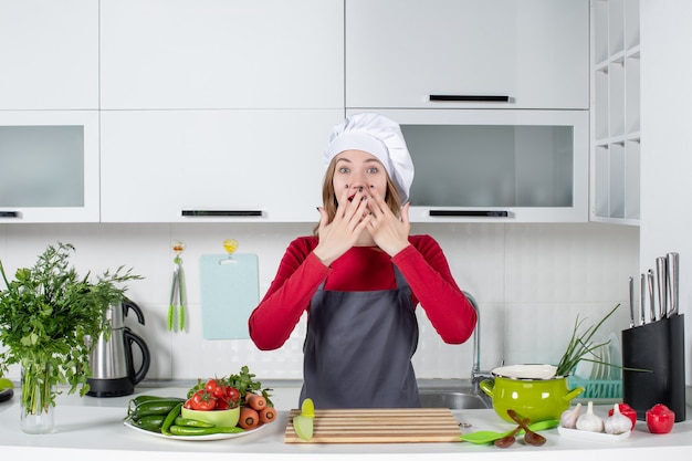 Vue de face jeune femme en tablier mettant les mains sur sa bouche