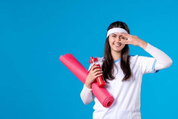 Vue De Face Jeune Femme Avec Tapis Pour Les Exercices Et Bouteille D'eau Sur Le Mur Bleu