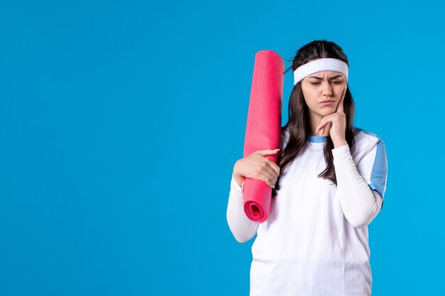 Vue de face jeune femme avec tapis pour exercices sur mur bleu