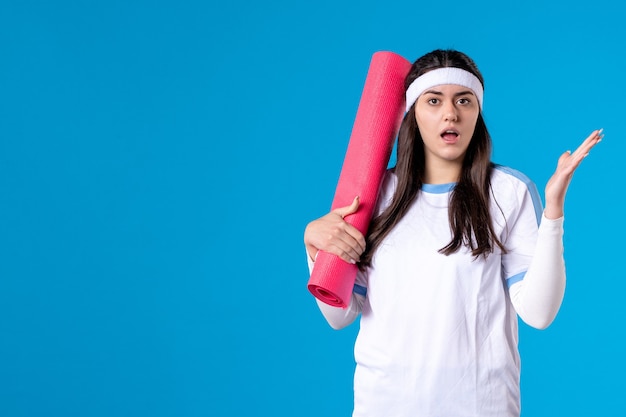 Vue de face jeune femme avec tapis pour exercices sur mur bleu