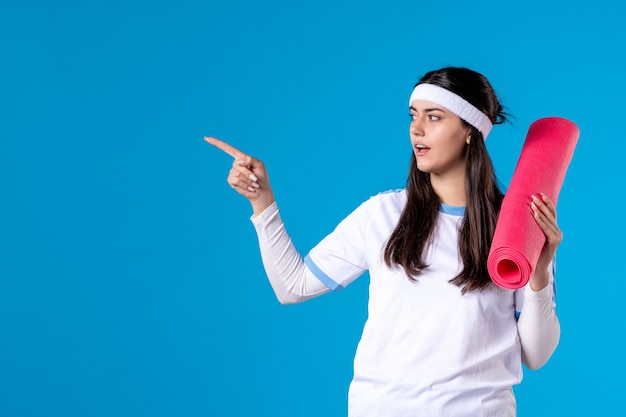 Vue de face jeune femme avec tapis pour exercices sur mur bleu