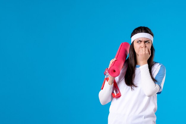 Vue de face jeune femme avec tapis de yoga sur mur bleu