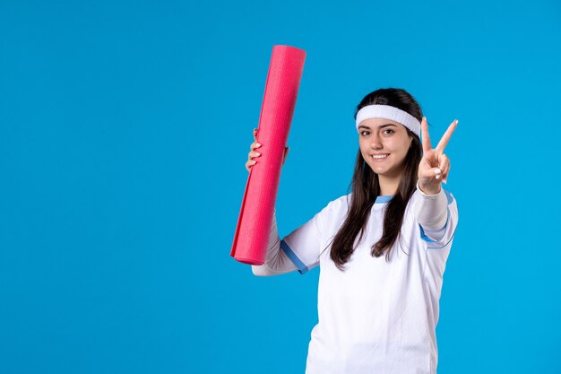 Vue de face jeune femme avec tapis de yoga sur mur bleu