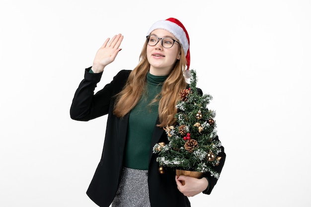 Vue de face jeune femme tenant arbre de vacances sur mur blanc jouet de Noël nouvel an