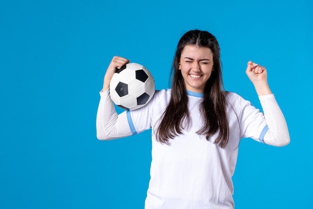 Vue de face jeune femme tenant un ballon de football sur un mur bleu