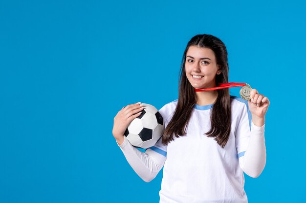 Vue de face jeune femme tenant un ballon de football sur un mur bleu