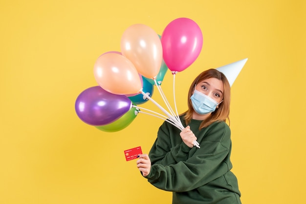 Vue de face jeune femme tenant des ballons colorés et carte bancaire