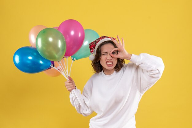 Vue de face jeune femme tenant des ballons colorés sur jaune