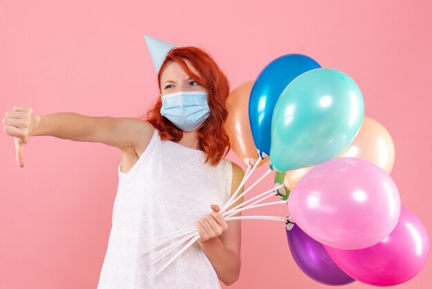 Vue de face jeune femme tenant des ballons colorés en masque sur le rose